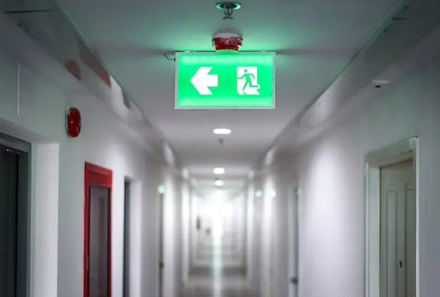 Pasillo de apartamentos con luz verde de emergencia que señala la salida segura